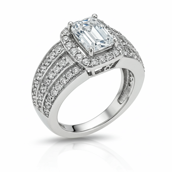 Men's white gold band, with the top part of the ring facing towards the upper left corner of the frame. The central element is a clear, emerald-cut gemstone, held in place by four prongs. Surrounding this central stone is a halo of smaller, clear, round gemstones. The band of the ring is wide and also heavily adorned with rows of small, clear, round gemstones, set closely together to create a sparkling effect. 